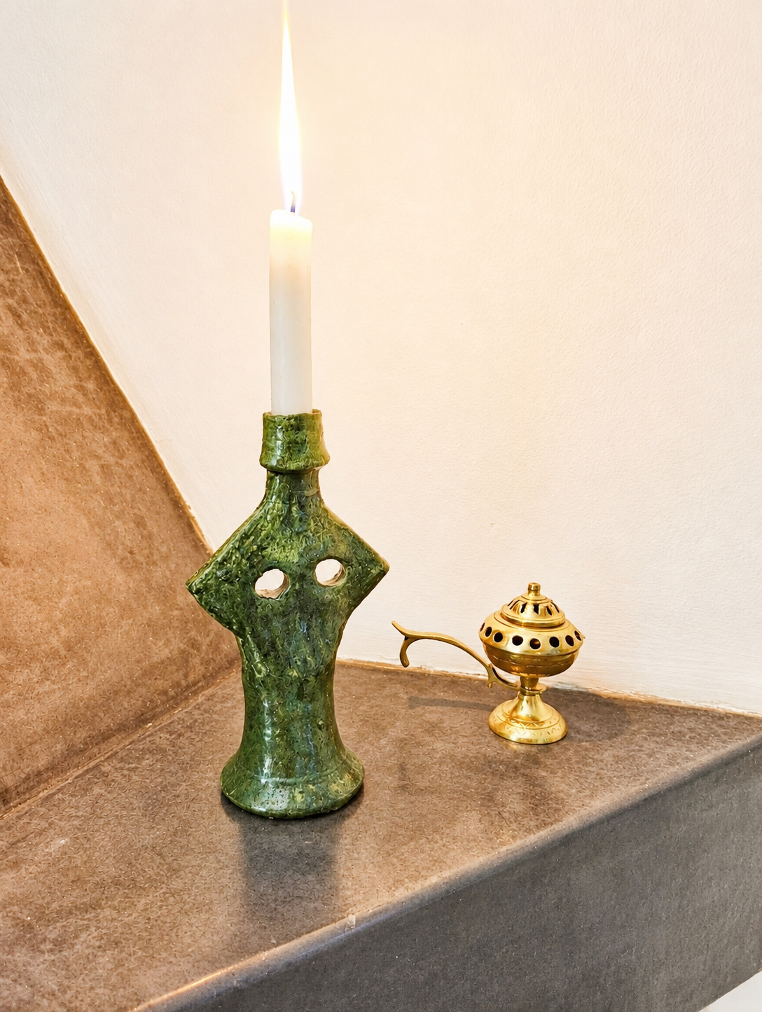 Traditional green Moroccan ceramic candle holder with a burning candle beside a brass incense burner on a stone shelf.